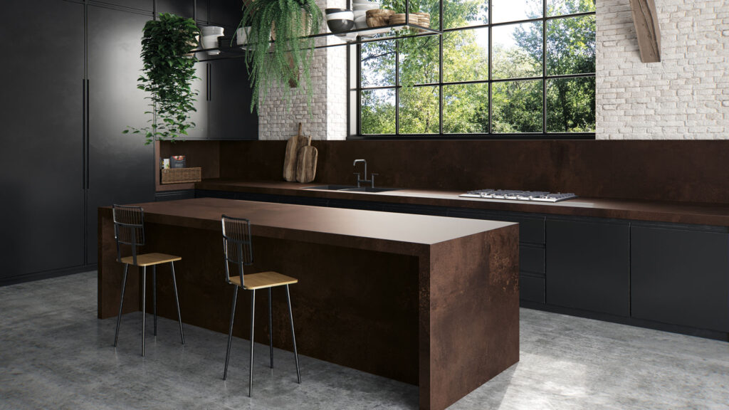 Caesarstone 303 - A modern kitchen features a brown island with two stools, dark cabinets, and hanging plants. Large windows provide a view of lush greenery, enhancing the bright, spacious atmosphere.