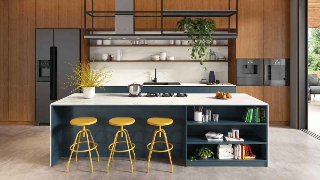 Caesarstone 501 - Kitchen island with yellow stools, marble top, and bookshelves, holding a vase with flowers. In a modern kitchen, a refrigerator and oven are against wooden walls; shelves display plants and dishes.