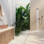 Caesarstone Porcelain 546 Thalassa in Outdoor shower area with plants, stone flooring, wooden vanity, round mirror, and copper sink.